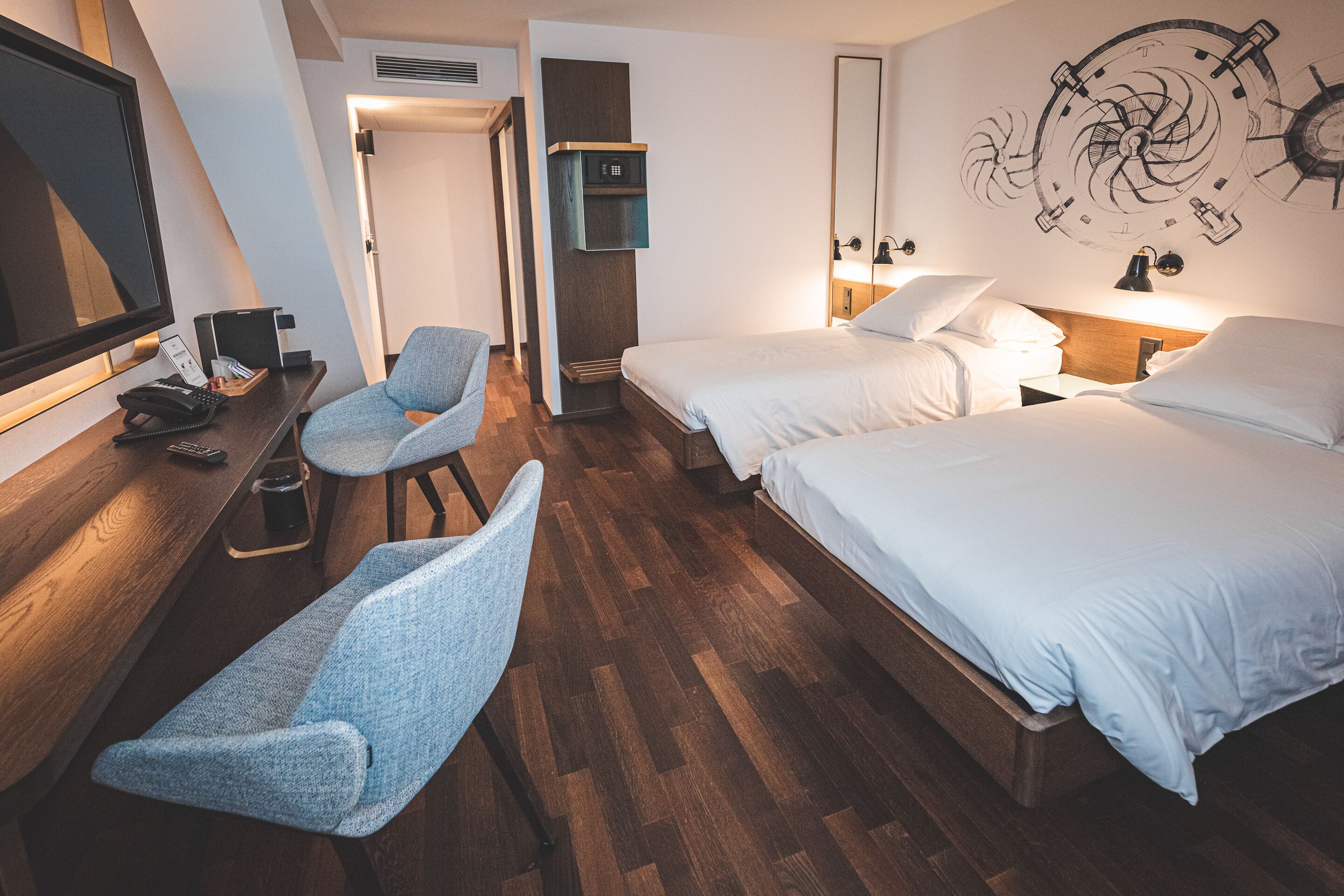 Habitación de hotel con dos camas, un escritorio con teléfono y una silla, televisión y un reloj de pared.