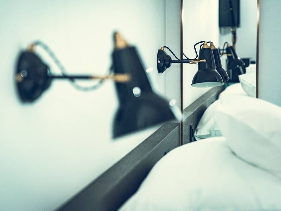 A hotel room with a bed, a nightstand, and two wall-mounted lamps.