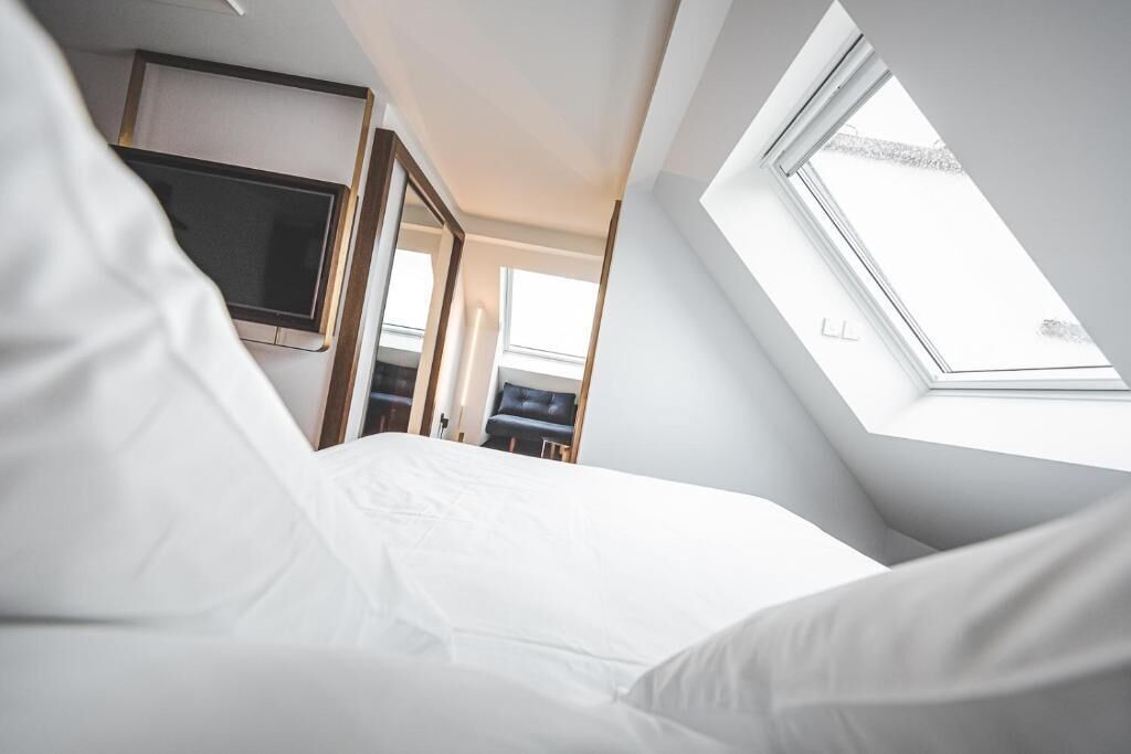 A bedroom with a skylight, a TV mounted on the wall, and a door leading to another room.