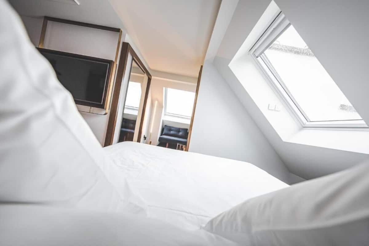 A bedroom with a skylight, a TV mounted on the wall, and a door leading to another room.