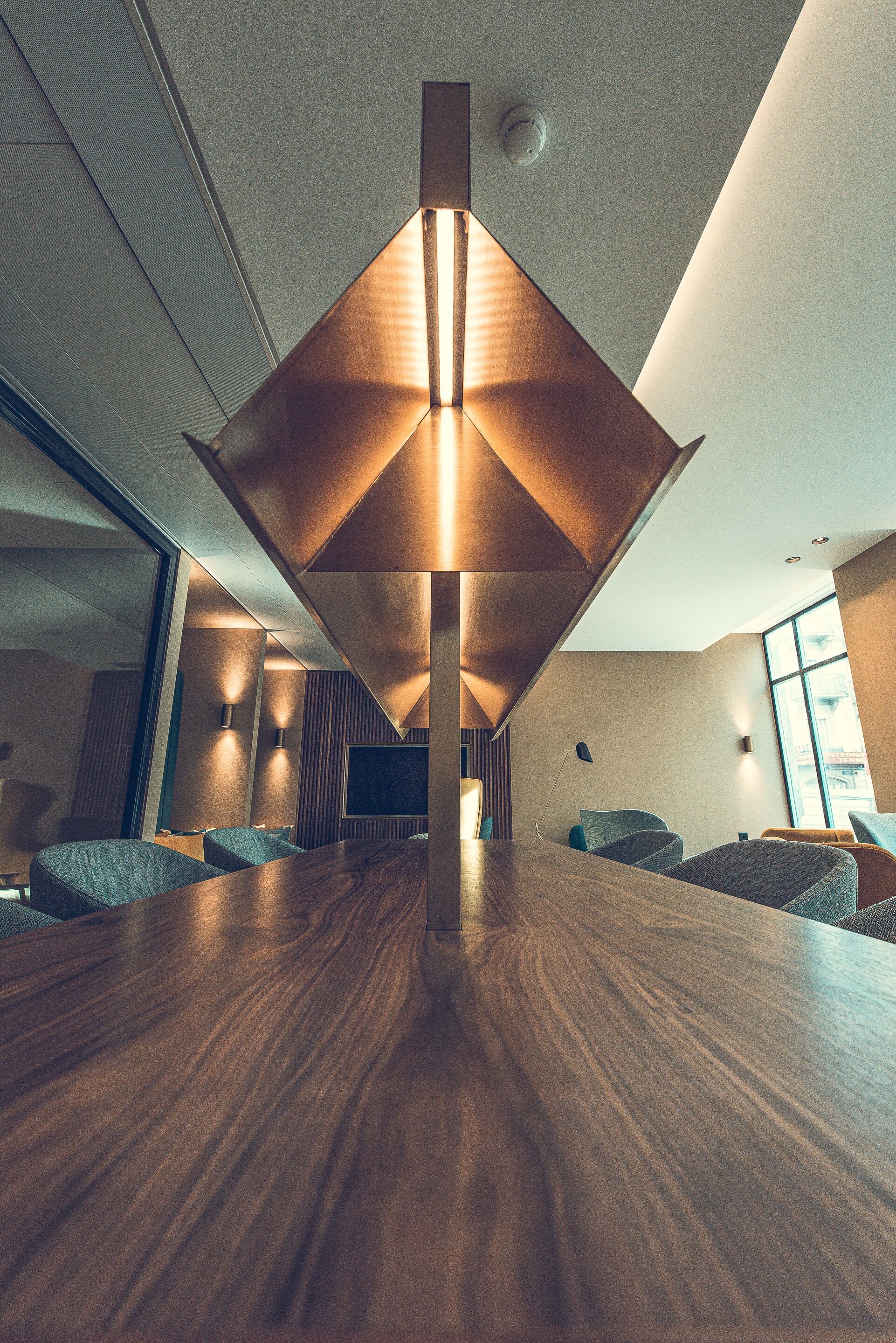 Una sala de conferencias moderna con una mesa de madera, asientos cómodos y una lámpara colgante de diseño geométrico.