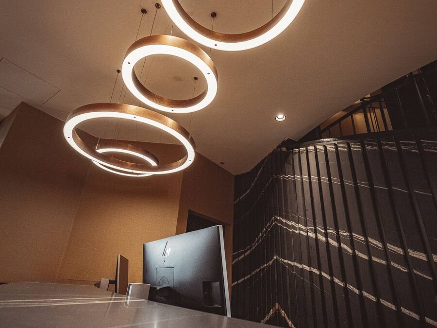 Un interior moderno con tres lámparas circulares en el techo, una pared de mármol y una escalera con diseño a rayas.