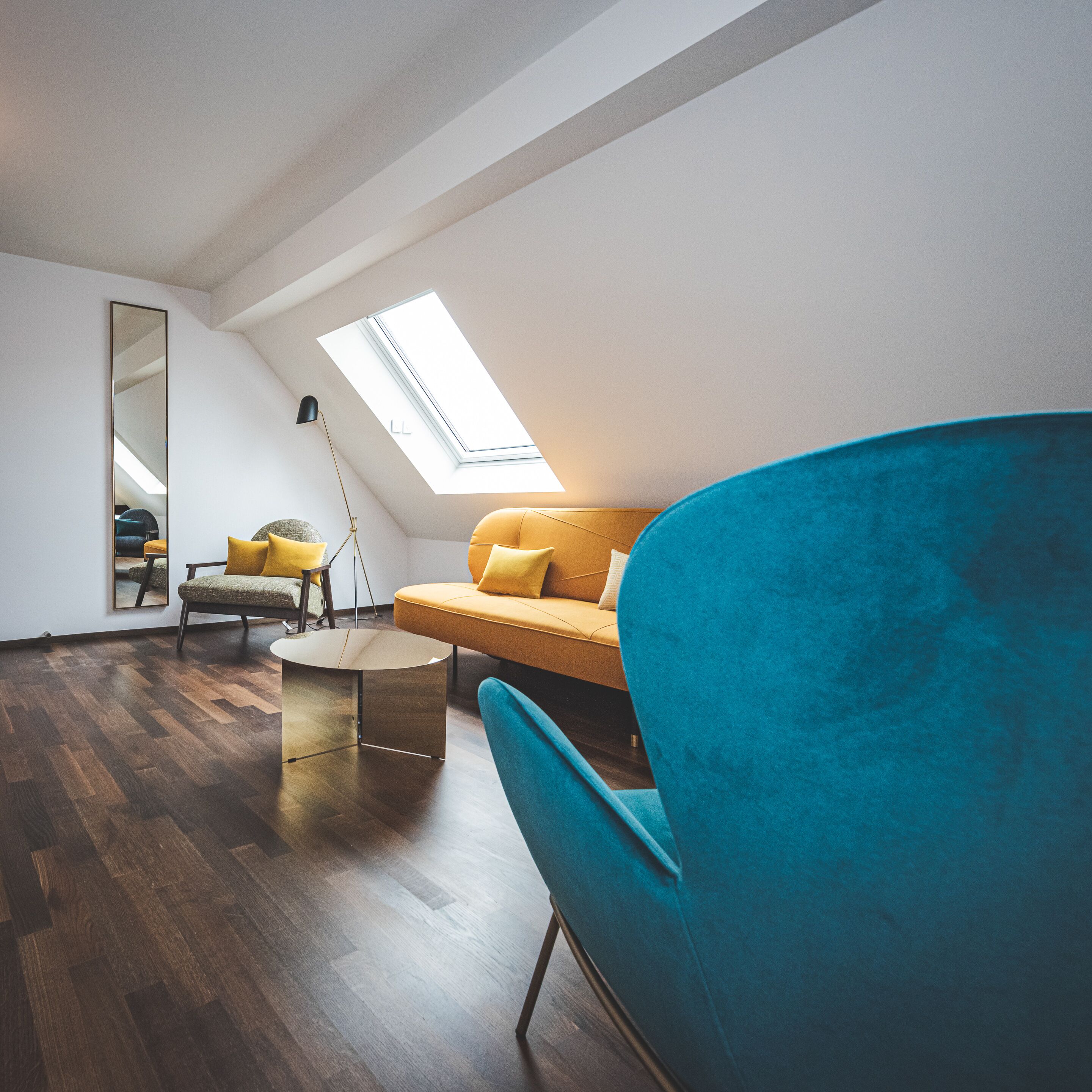A modern loft bedroom with a skylight, a round coffee table, a sofa, and a blue armchair.