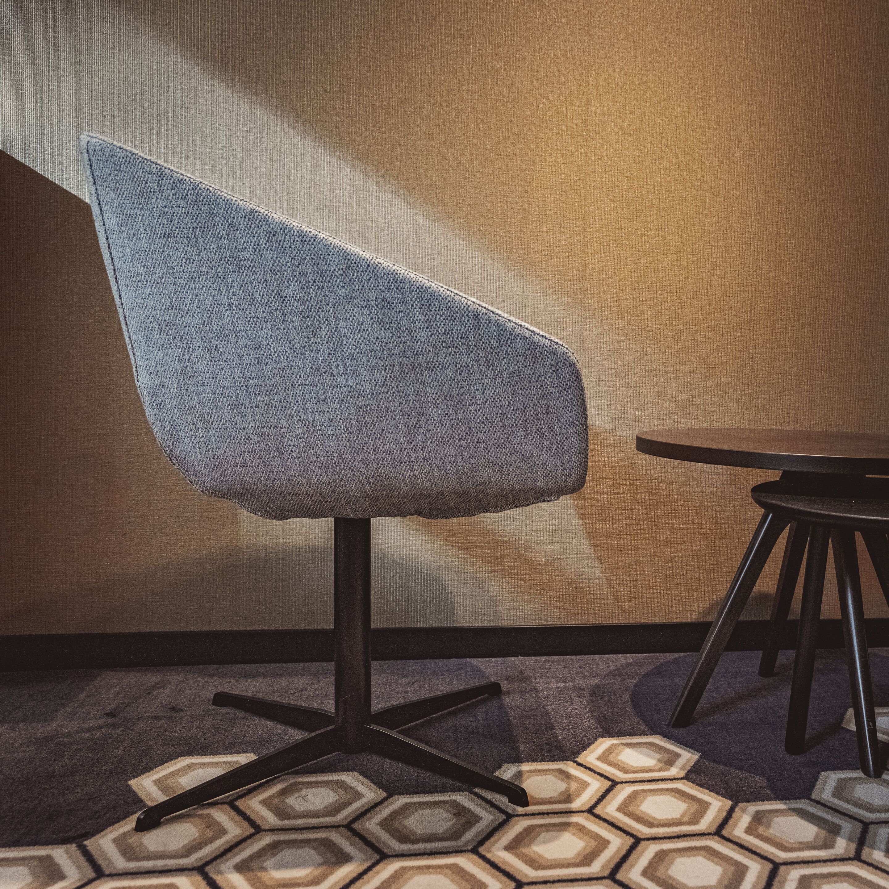A chair with a textured fabric backrest and a black metal base, positioned on a patterned carpet with hexagonal designs.