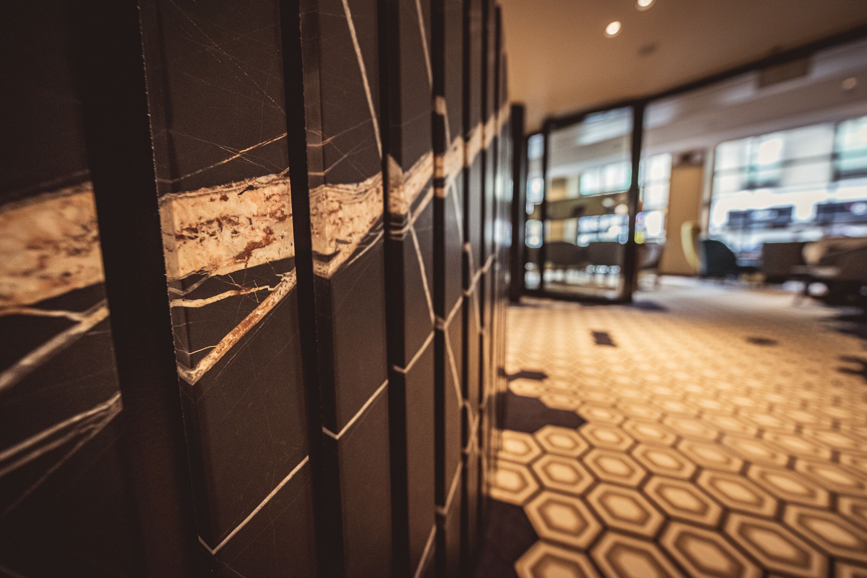 A corridor with marble walls and a patterned floor, leading to a modern interior space with glass partitions and seating areas.