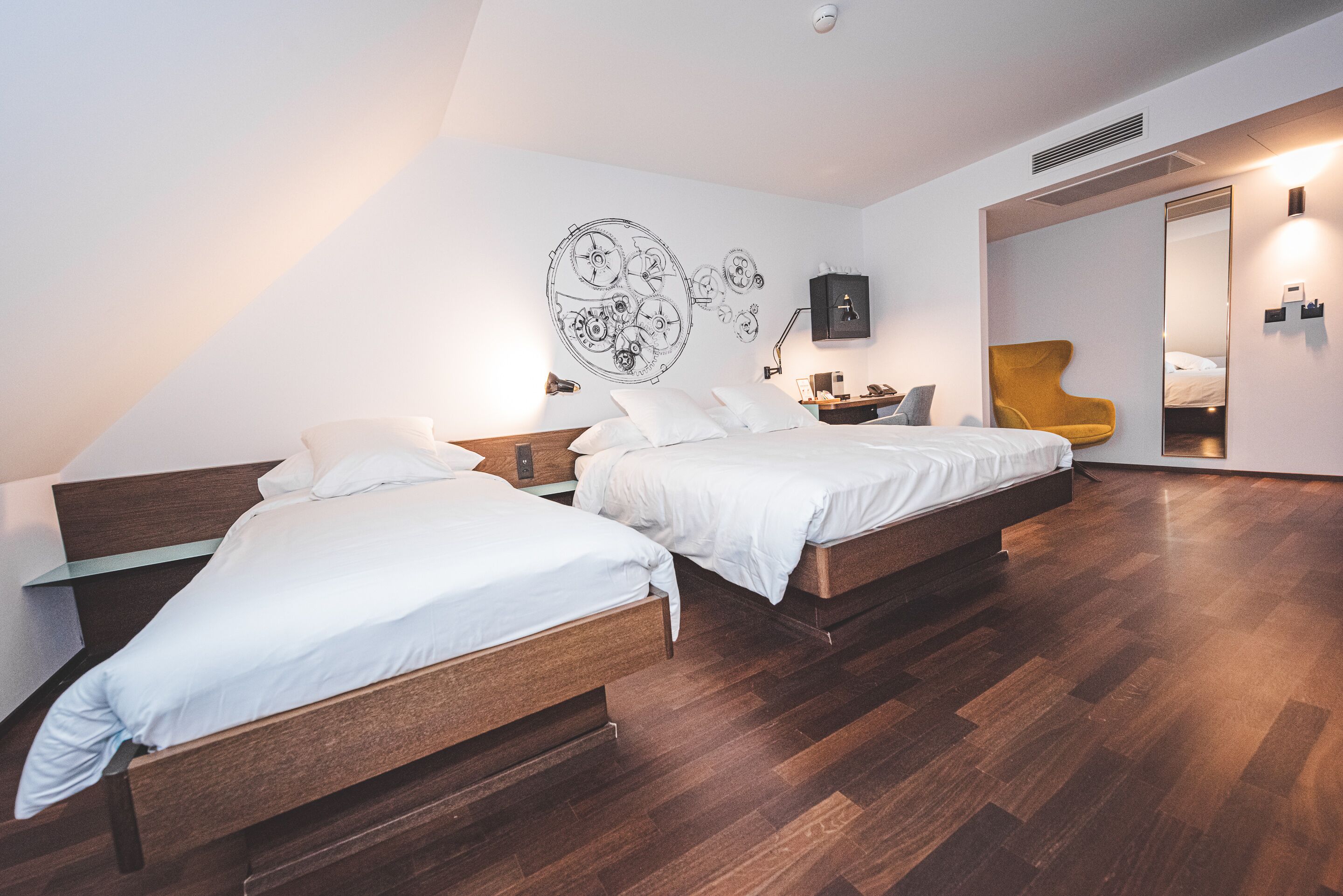 A modern bedroom with two wooden beds, a wall clock mural, a mirror, and a yellow chair.