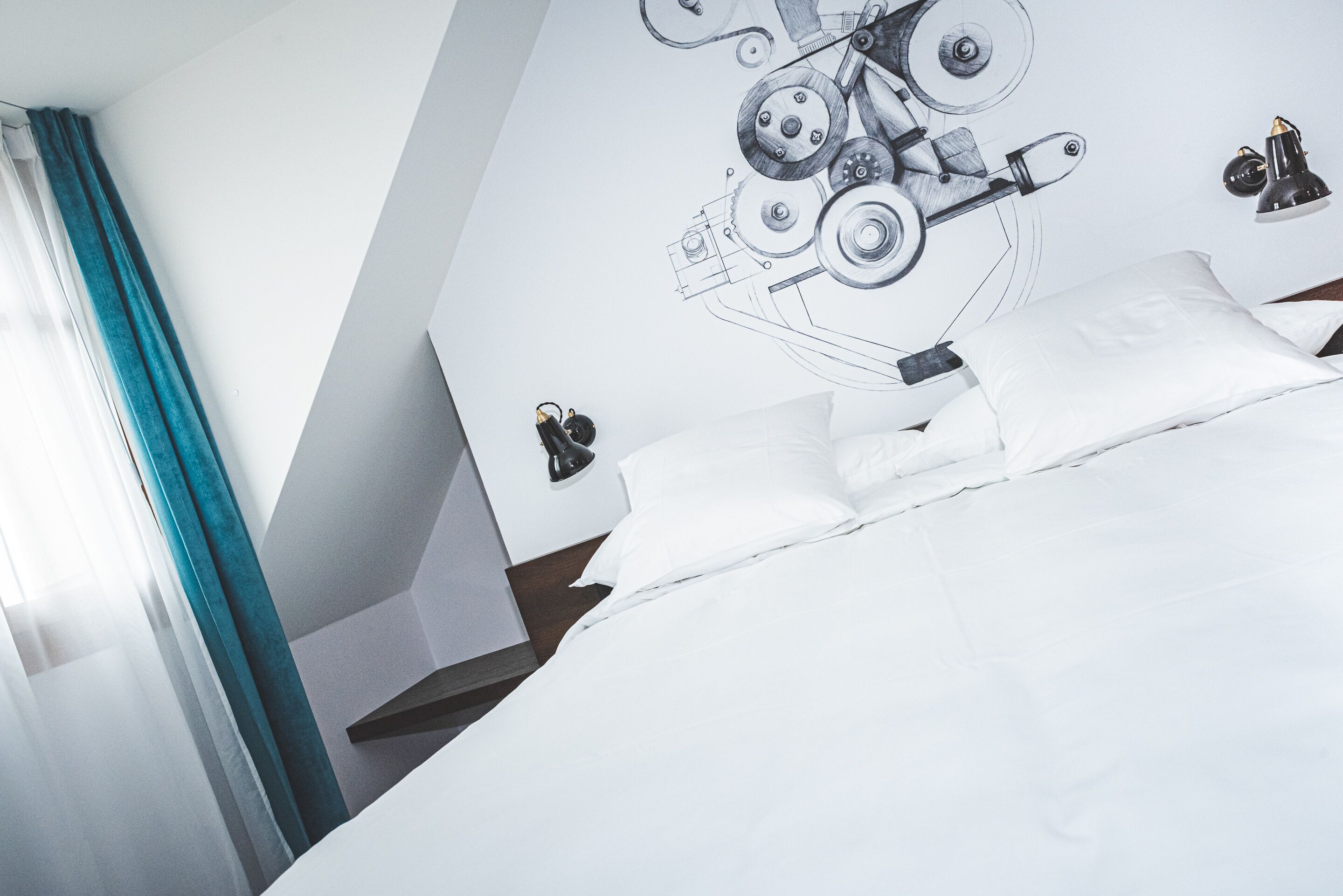 A modern hotel room with a bed, white linens, a wall-mounted mechanical drawing, and a nightstand with a lamp.