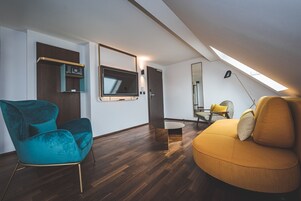 Una sala de estar moderna con suelo de madera, un sillón verde azulado, un sofá amarillo, un televisor de pantalla plana y un tragaluz.