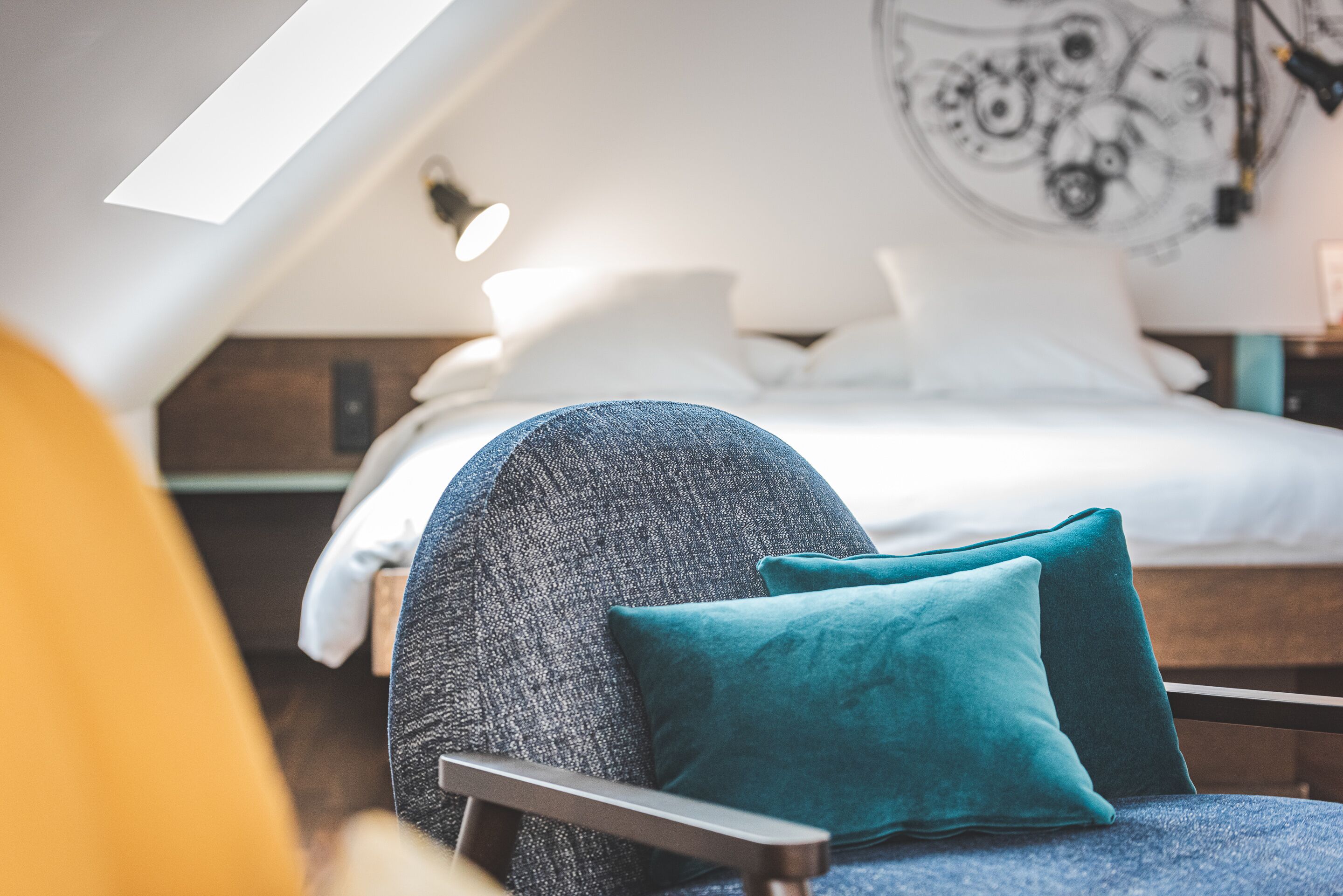 A modern bedroom with a loft-style ceiling, a bed with white linens, and teal pillows.