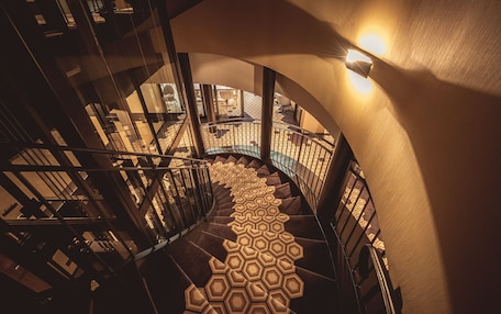 A spiral staircase with a geometric patterned floor, surrounded by walls with a smooth texture and a light fixture on the wall.