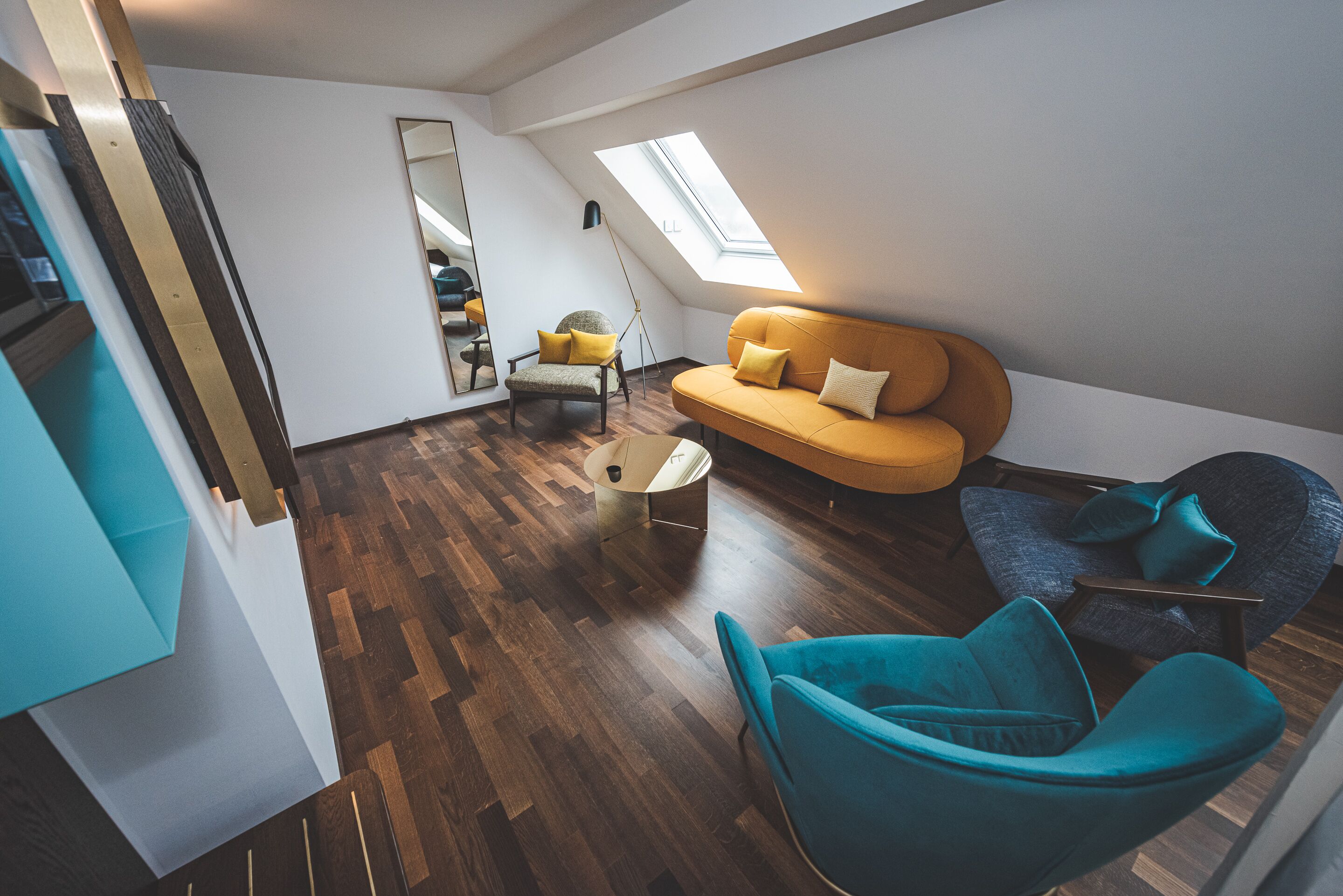 Eine moderne Loftswohnung mit Holzboden, einer Couch, zwei Sesseln, einem kleinen Couchtisch und einem Oberlicht.