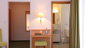 Une chambre d’hôtel équipée d’un bureau, d’une chaise, d’une lampe et d’une salle de bain visible à travers une porte ouverte.