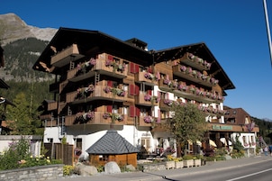 Un hotel de varios pisos con balcones decorados con flores, un letrero de restaurante y montañas al fondo.