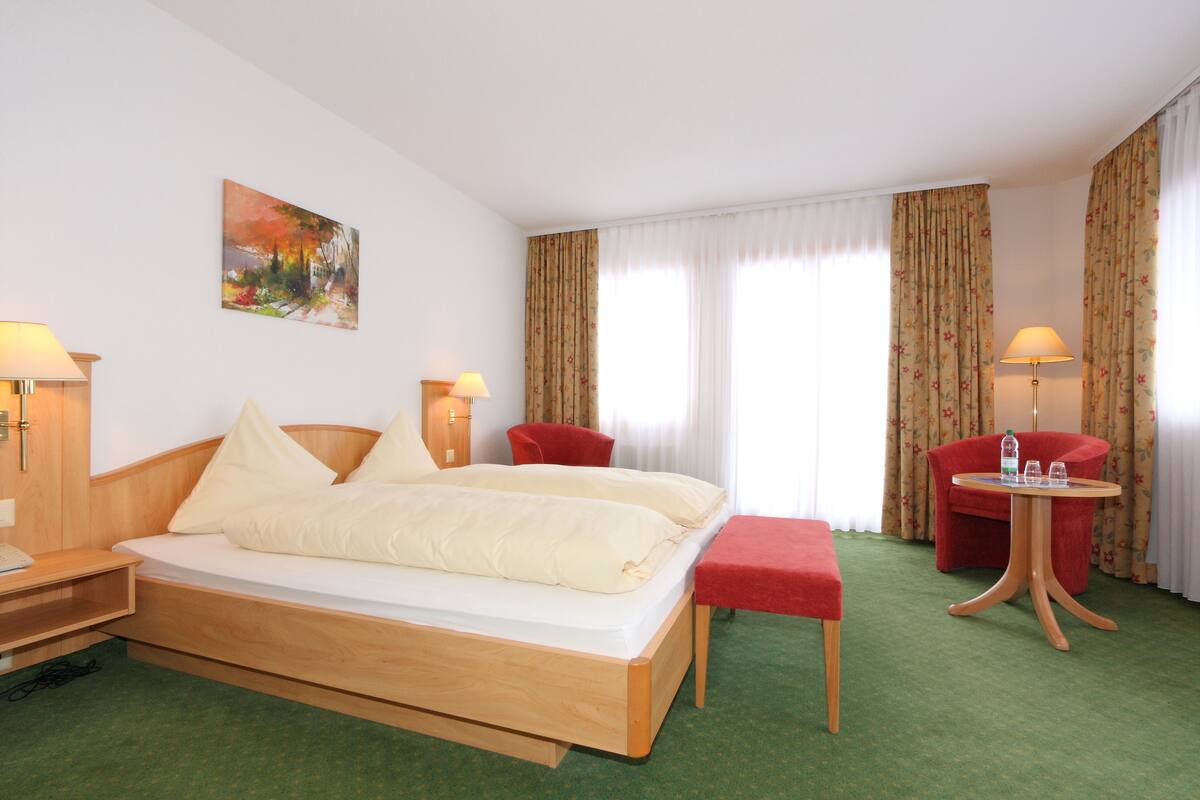 A hotel room with a wooden bed, a red armchair, a small round table, and a painting on the wall.