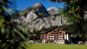Un hotel de varios pisos, con balcones adornados con macetas de flores y montañas al fondo.