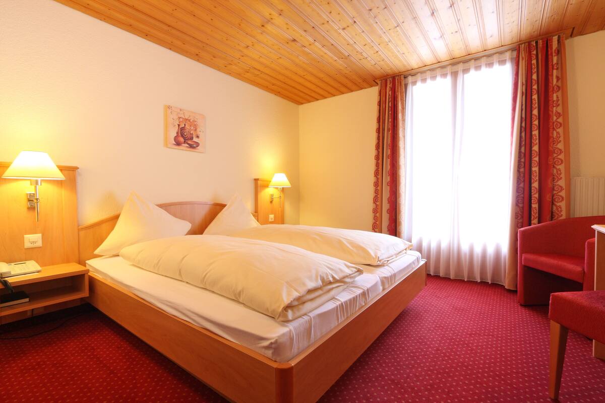 A hotel room with a wooden bed, two bedside lamps, a red carpet, and a red chair.