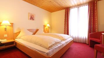 A hotel room with a wooden bed, two bedside lamps, a red carpet, and a red chair.