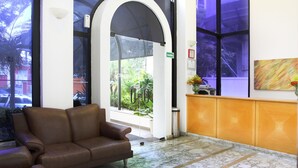 Un vestíbulo con un sofá de cuero marrón, un mostrador de recepción con un florero y grandes ventanales que ofrecen vistas al exterior.