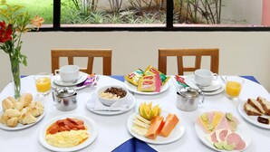 Una mesa de desayuno con diversos alimentos, un preparativo para café y vistas al verdor a través de una ventana.