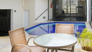 Zona de piscina con sillas de mimbre y una mesa de vidrio, un extintor y una puerta que da a un espacio interior.