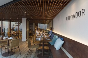 A restaurant with a long communal dining table, individual tables, wicker chairs, and a wall with the name "ARPOADOR".