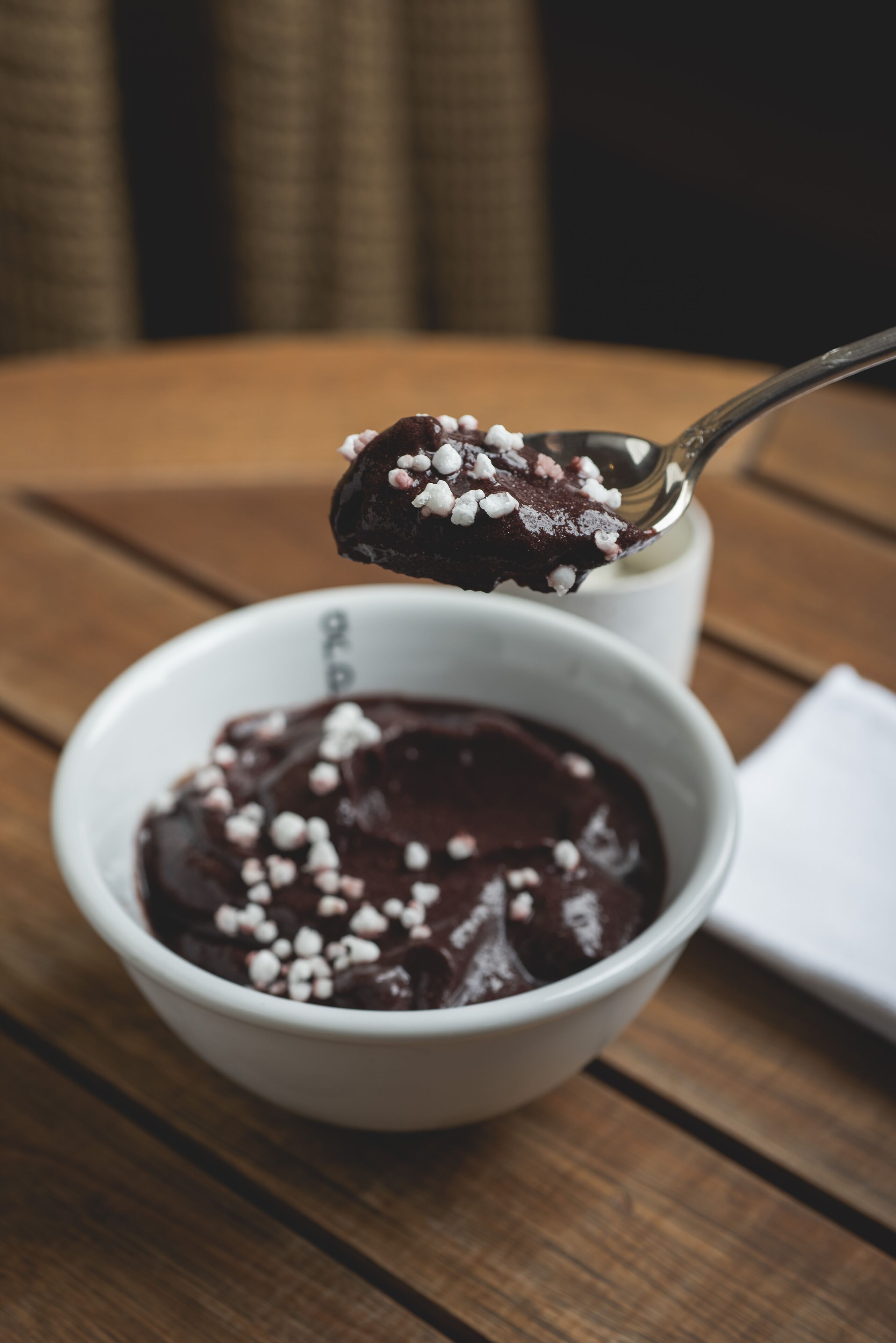 Uma colherada de sobremesa de chocolate com confeitos brancos sendo retirada de uma tigela branca.