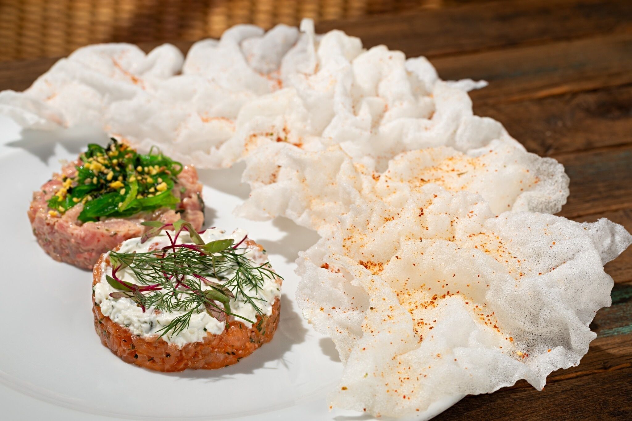 A plate with food items, including a salmon tartare and a creamy dish garnished with herbs.