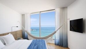 Habitación de hotel con un ventanal grande, cama, televisor y mesita de noche.