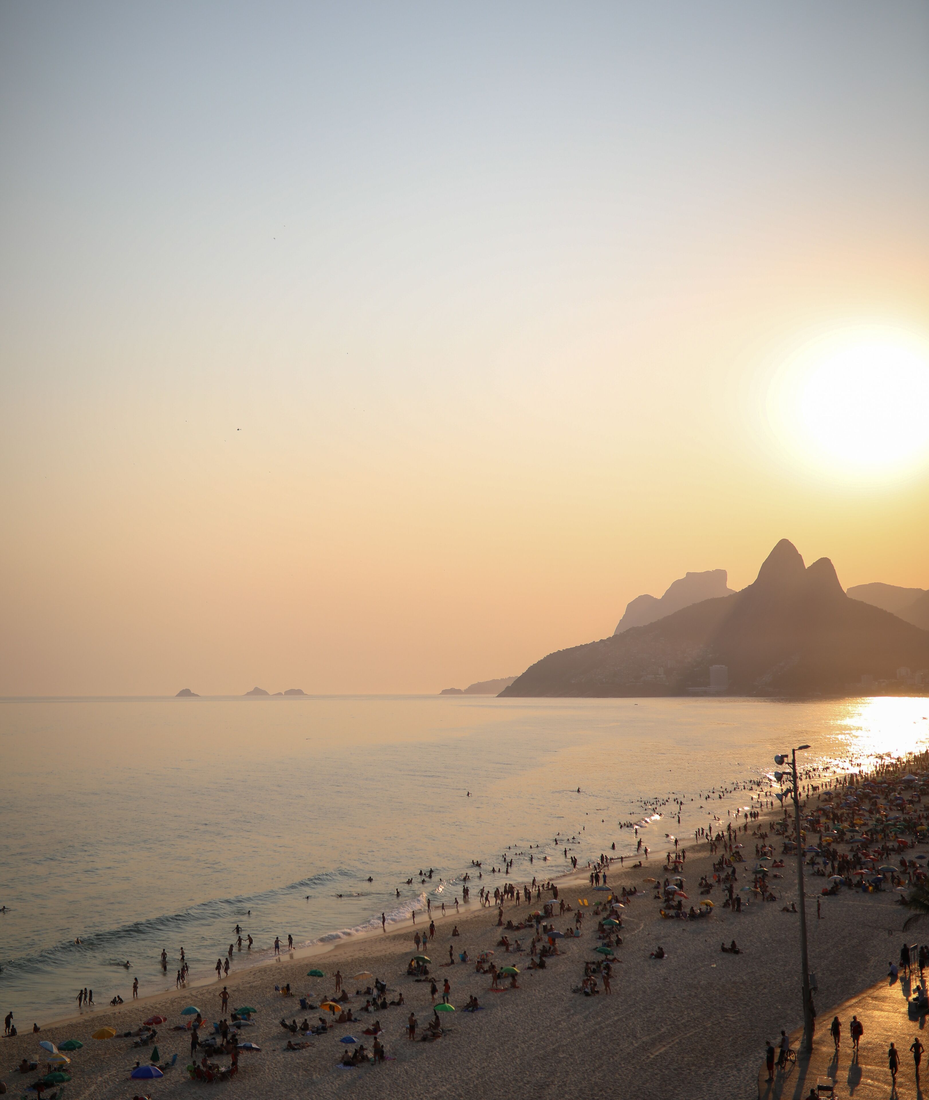 Een strand met mensen, parasols en een zonsondergang.