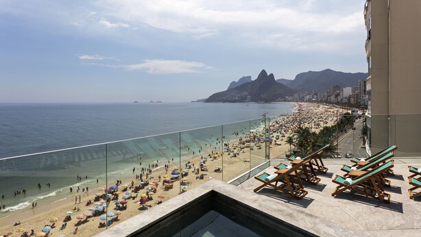 A poolside view overlooking a beach with lounge chairs and umbrellas. - Hotel Arpoador (Rio de Janeiro)