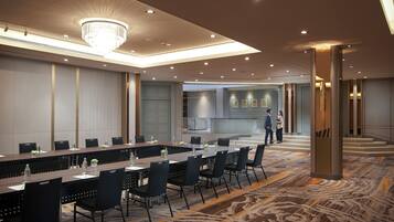 A conference room with a long table, chairs, and a chandelier. There are two people standing near a staircase.
