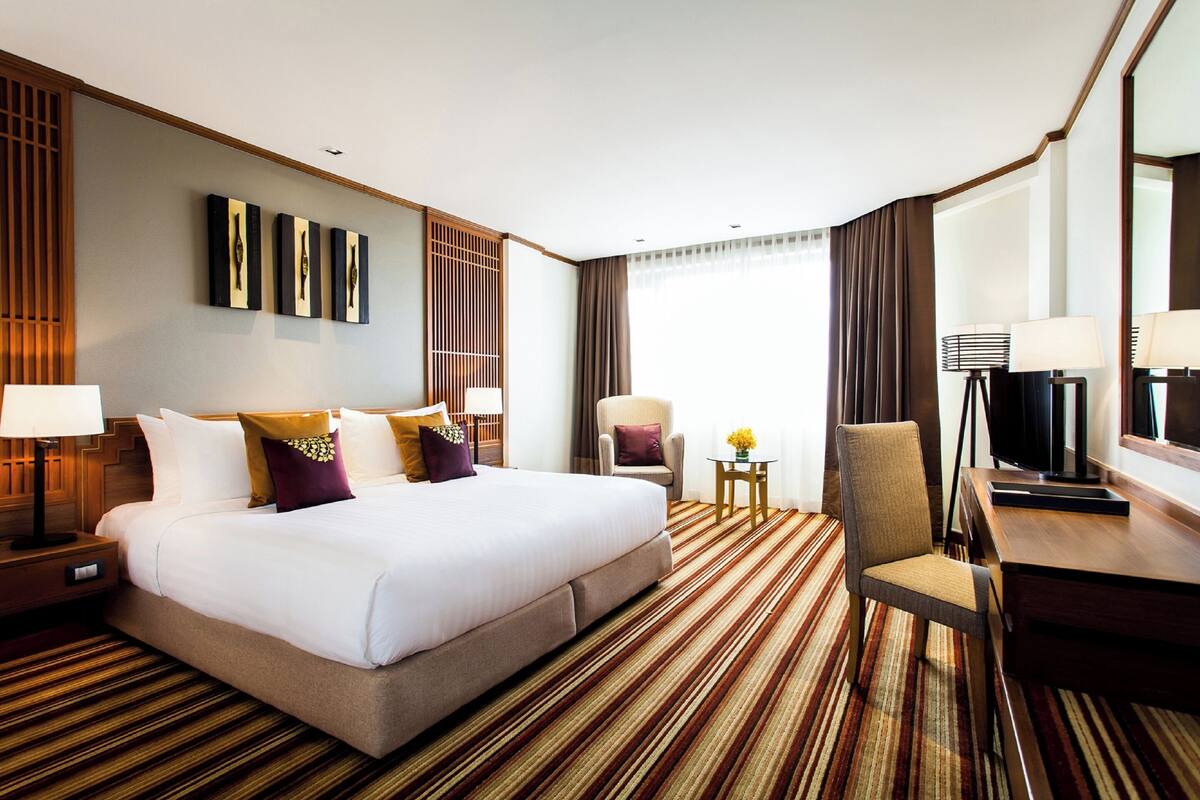 Habitación de hotel con una cama grande, un escritorio, una silla, un televisor y una mesita de noche con lámpara.