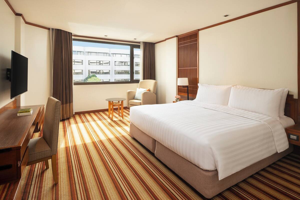 Habitación de hotel con una cama grande, un escritorio, una silla, un televisor y una ventana con vistas a edificios.