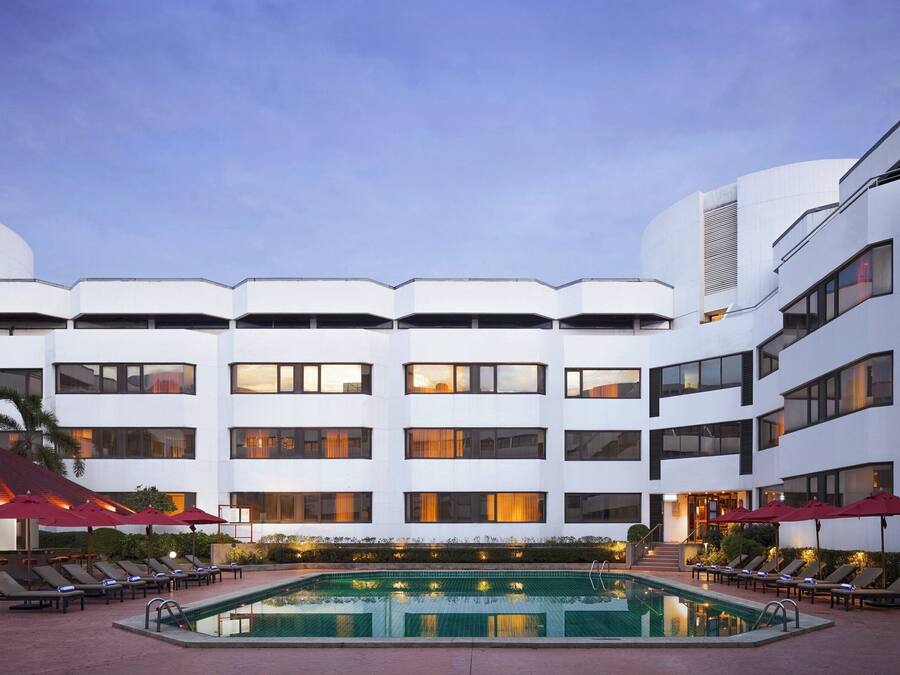 Un hôtel moderne doté d’une piscine, de plusieurs étages et d’un espace extérieur aménagé avec des parasols.