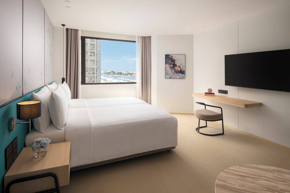 Habitación de hotel con cama, escritorio con lámpara, una silla, televisor y ventana con vista a la ciudad.
