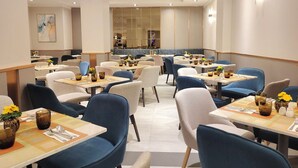 Un espace de restauration moderne avec plusieurs tables et chaises, une cuisine en arrière-plan et une palette de couleurs neutres.