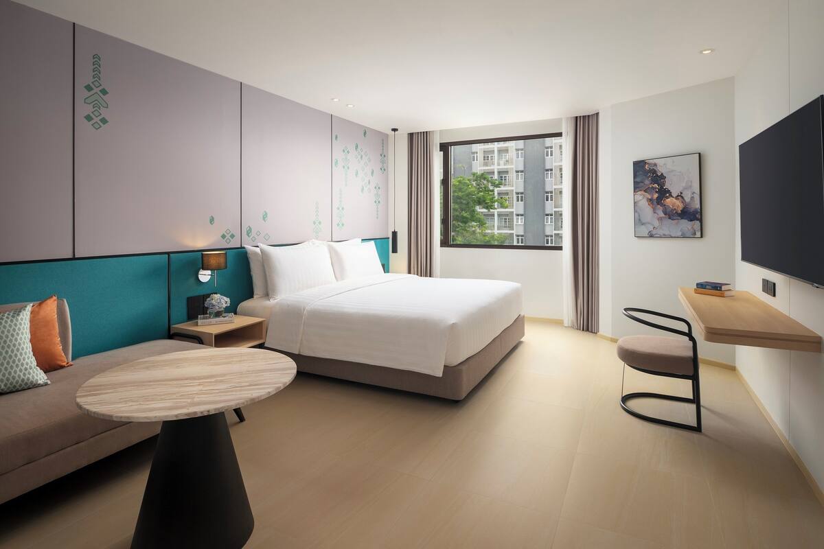 Una habitación de hotel moderna con cama, sofá, mesita, escritorio y televisor.