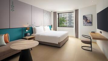 Una habitación de hotel moderna con cama, sofá, mesita, escritorio y televisor.