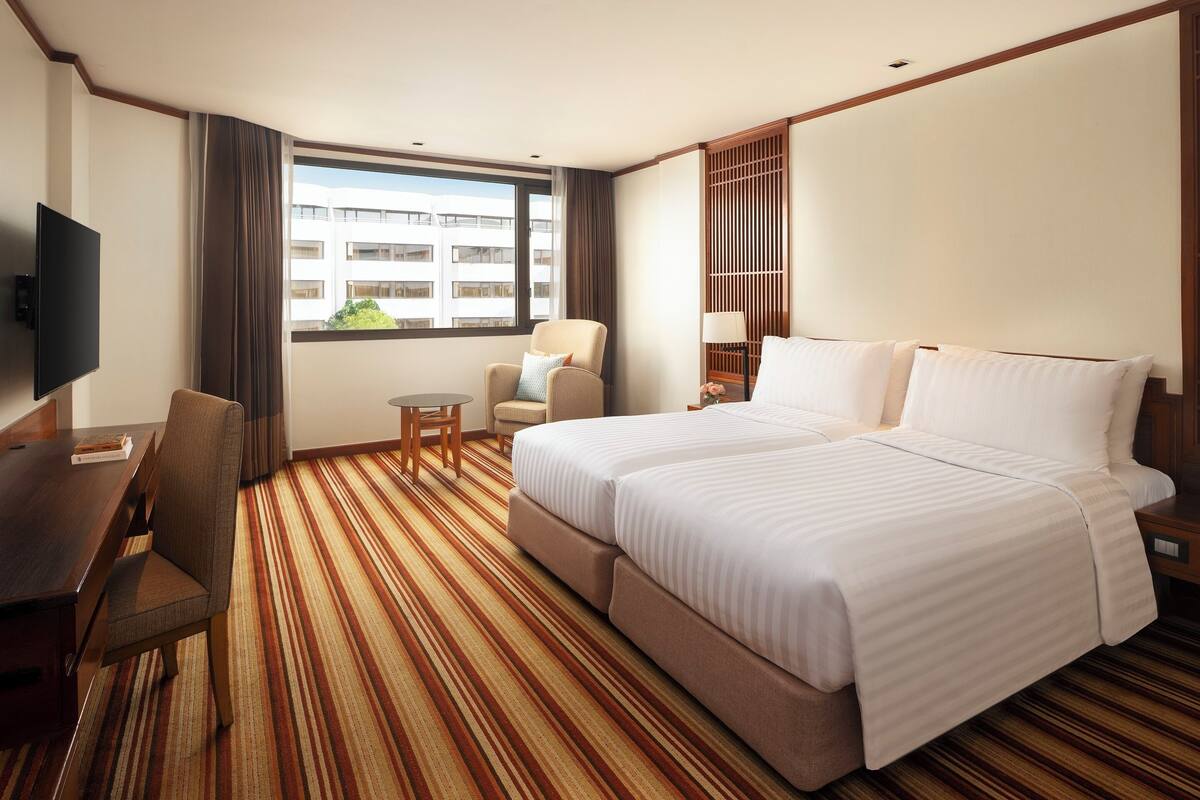 Habitación de hotel con cama, escritorio, silla, televisor y ventana con vistas a edificios.