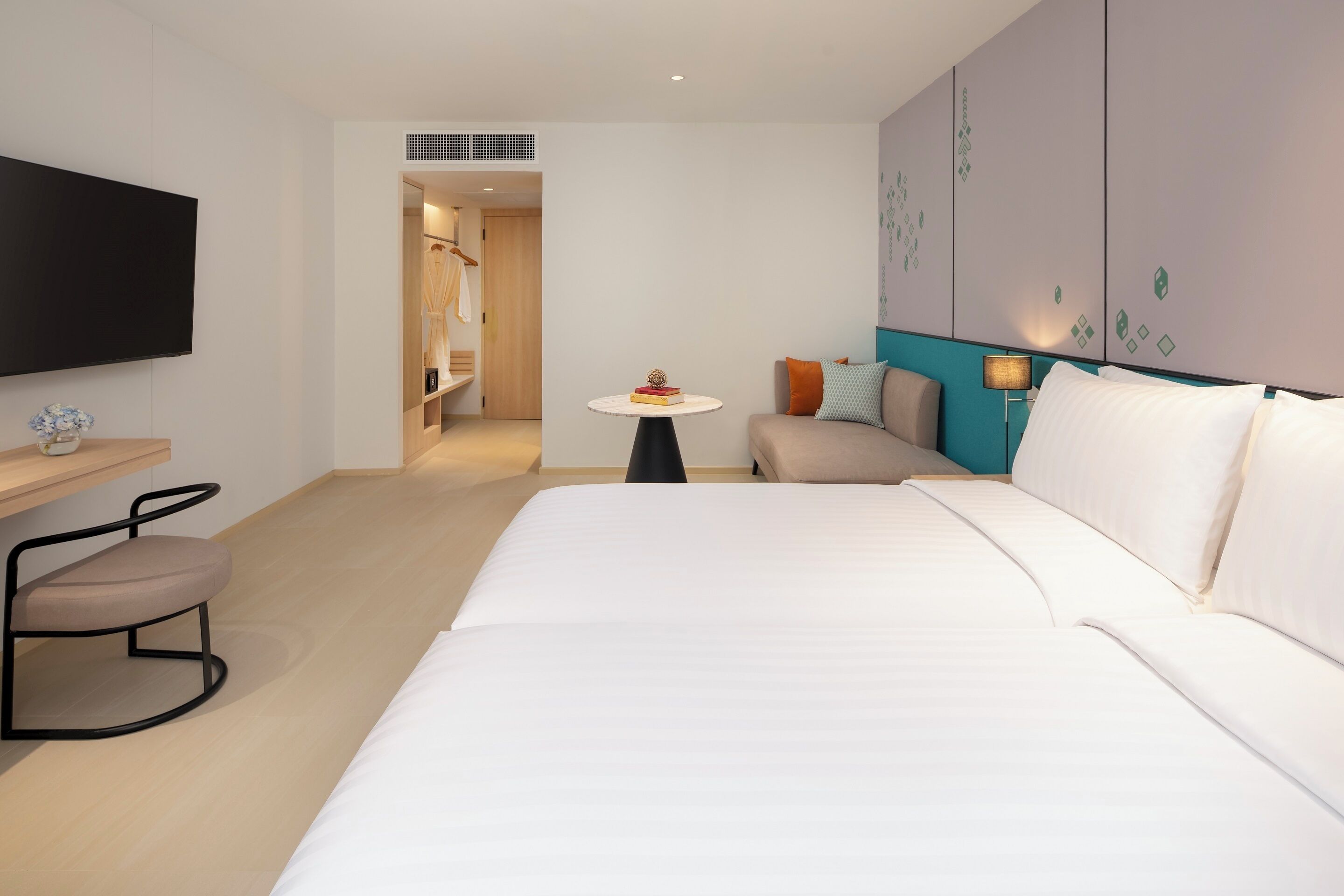 Una habitación de hotel con cama, televisión, escritorio con silla, una mesita con lámpara y armario.