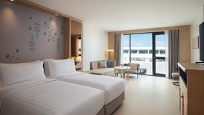 Habitación de hotel con dos camas, un sofá, una mesita y un televisor.