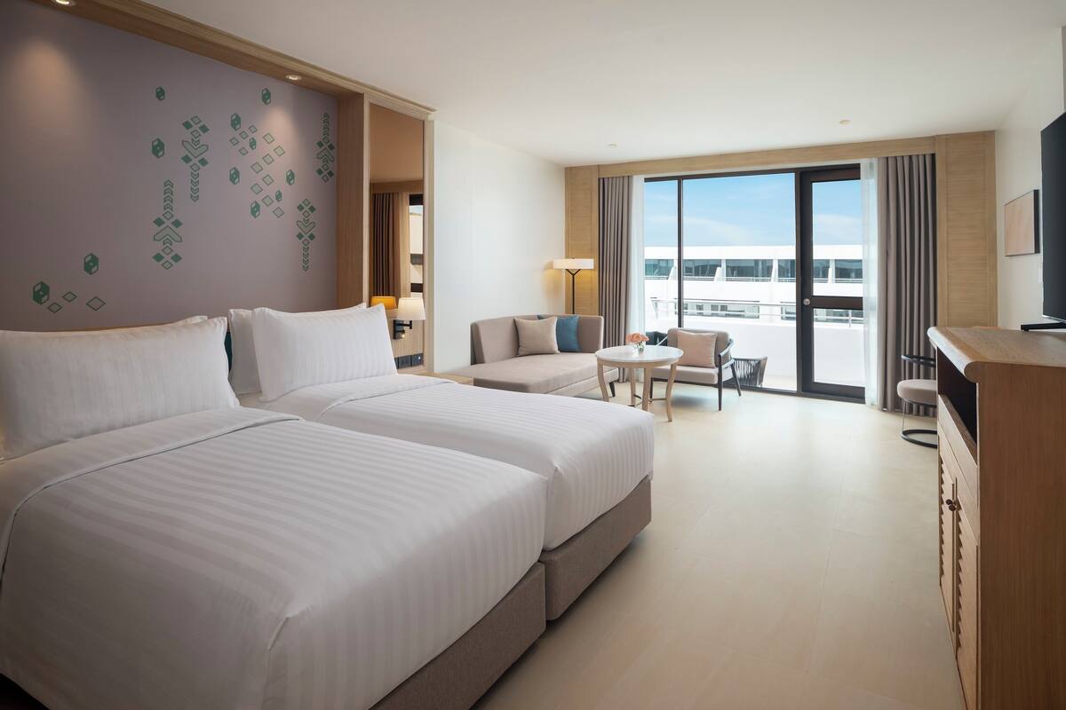 Habitación de hotel con dos camas, un sofá, una mesita y un televisor.