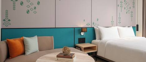 Habitación de hotel con cama, sofá, mesa redonda con un libro y pared con patrones geométricos.