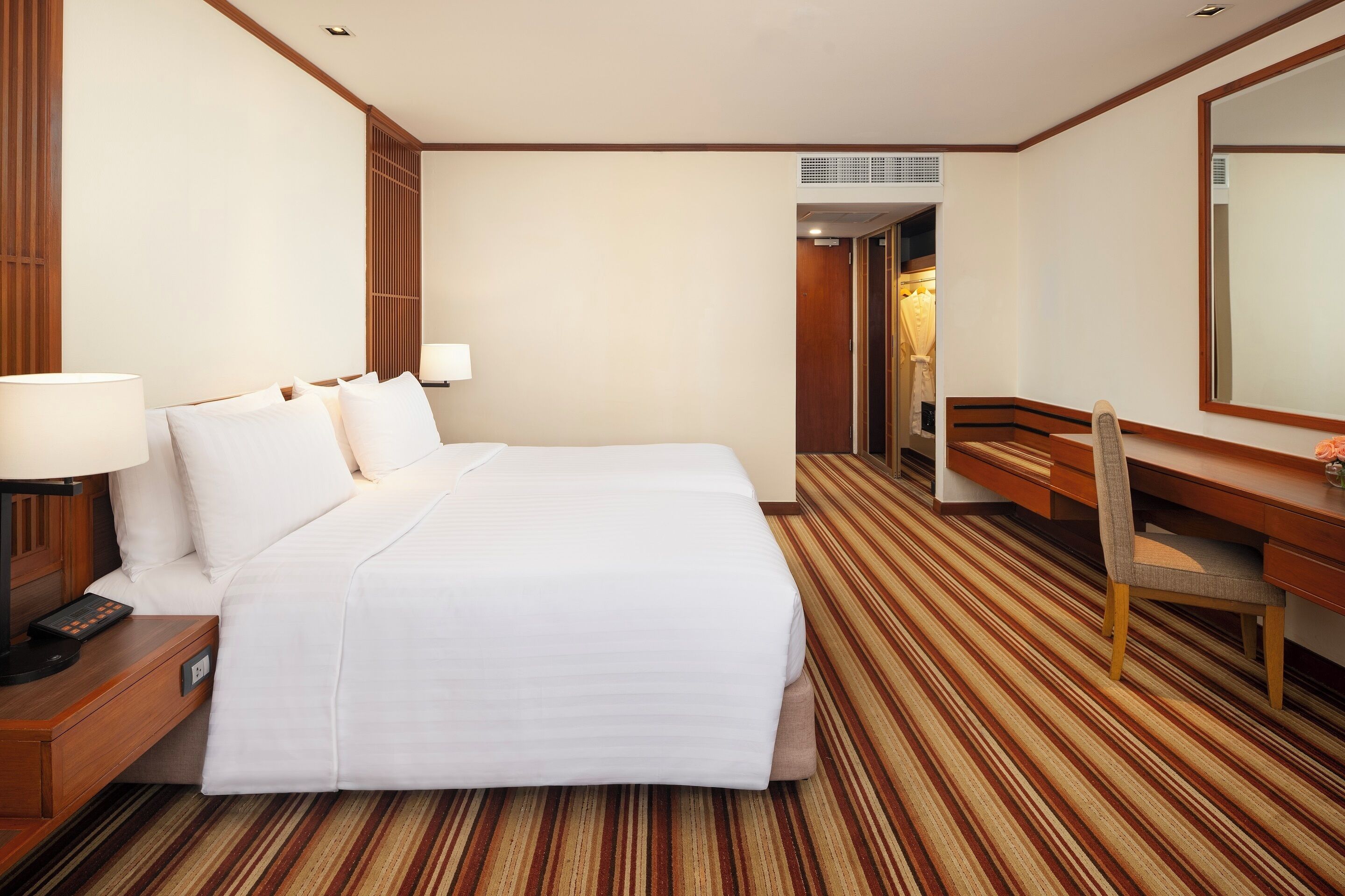 A hotel room with a bed, bedside table, lamp, desk, chair, and a large mirror.