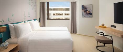 Een hotelkamer met twee bedden, een televisie, een bureau en een raam met uitzicht op gebouwen.