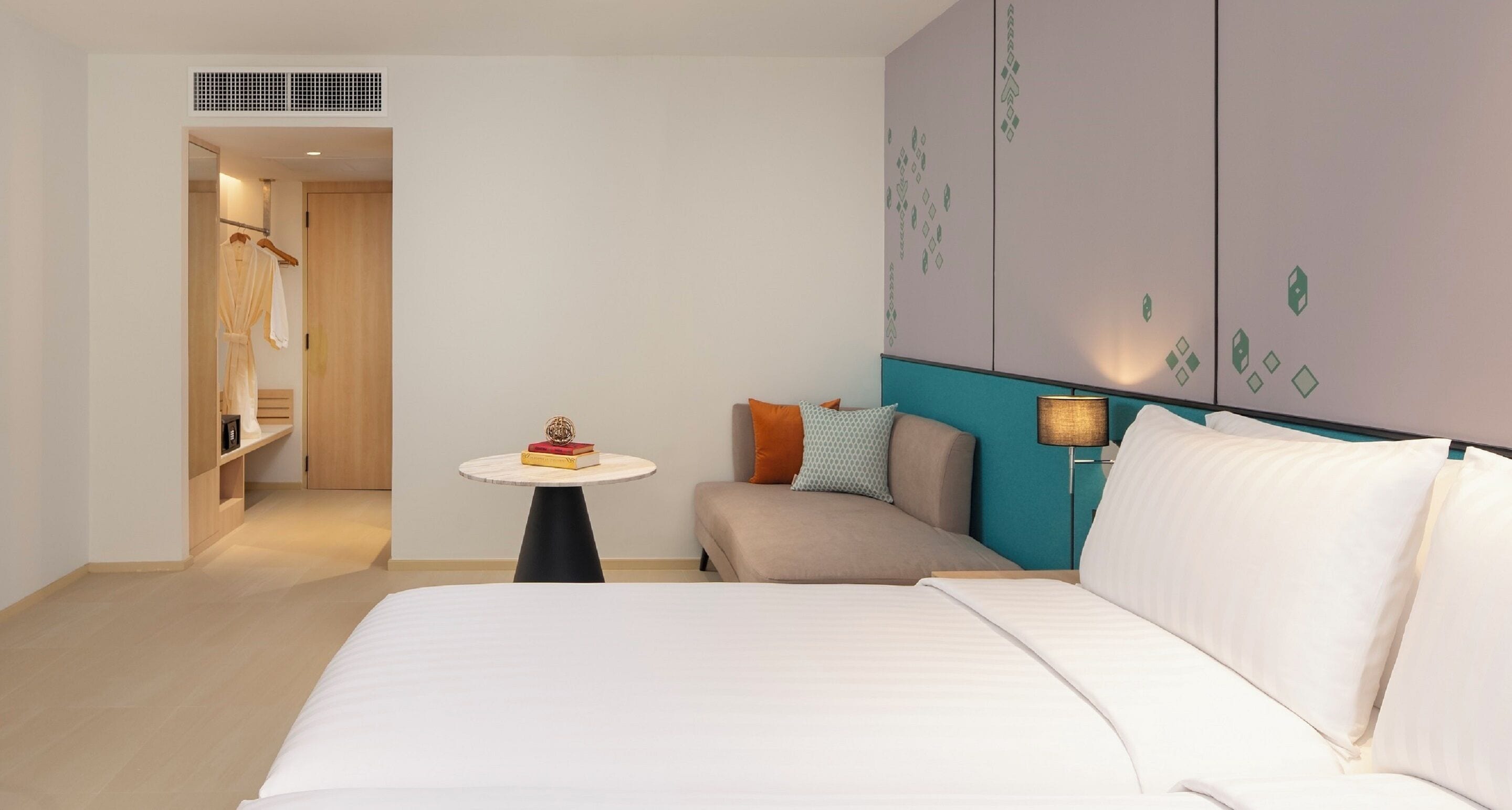 Una habitación de hotel con una cama, una pequeña mesa con libros, un sofá y una lámpara.