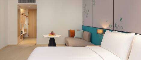 Una habitación de hotel con una cama, una pequeña mesa con libros, un sofá y una lámpara.