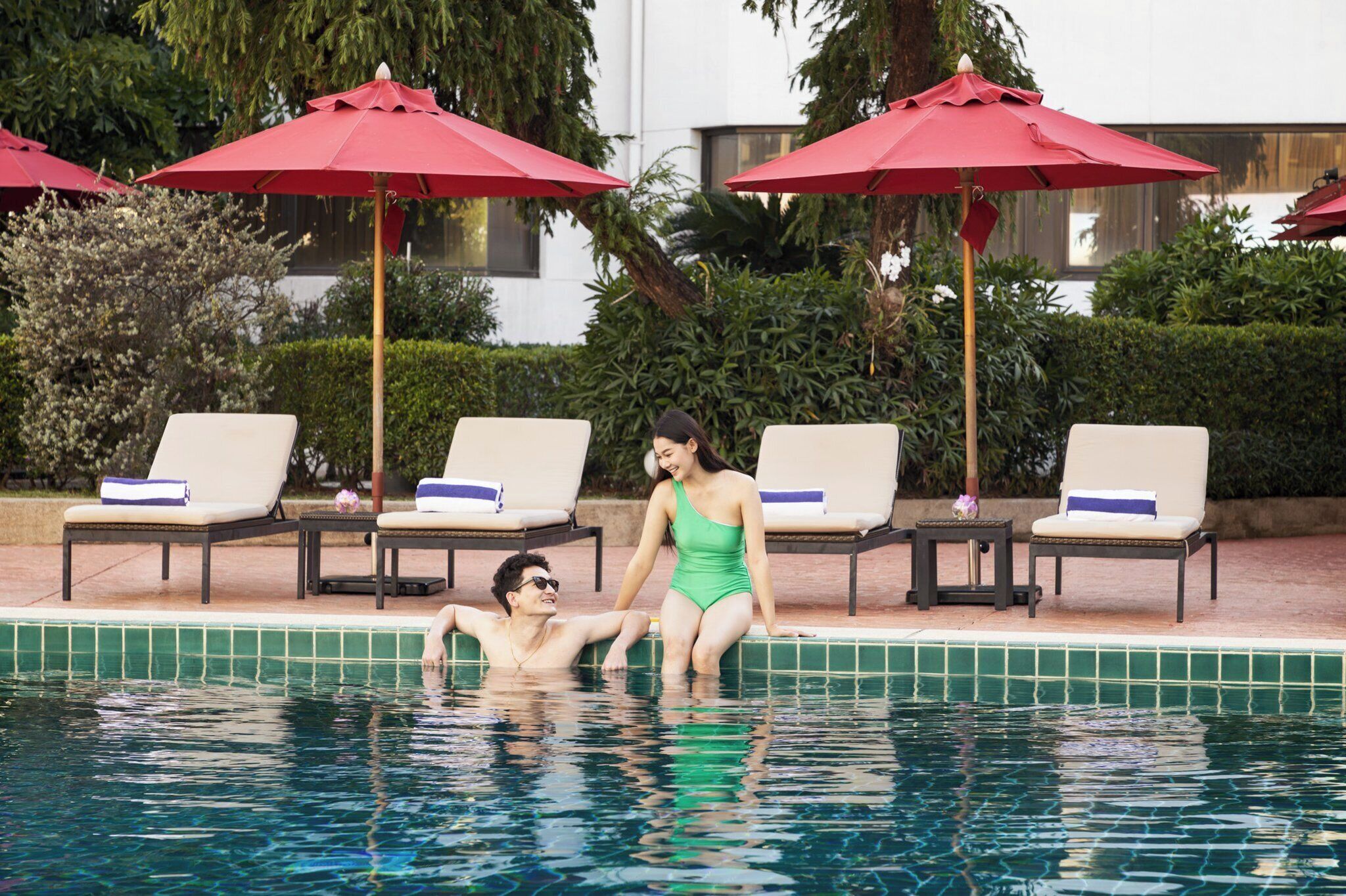 A poolside area with lounge chairs and red umbrellas.