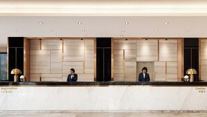 Mostrador de recepción de hotel con dos empleados, una zona de registro y una sección de caja.