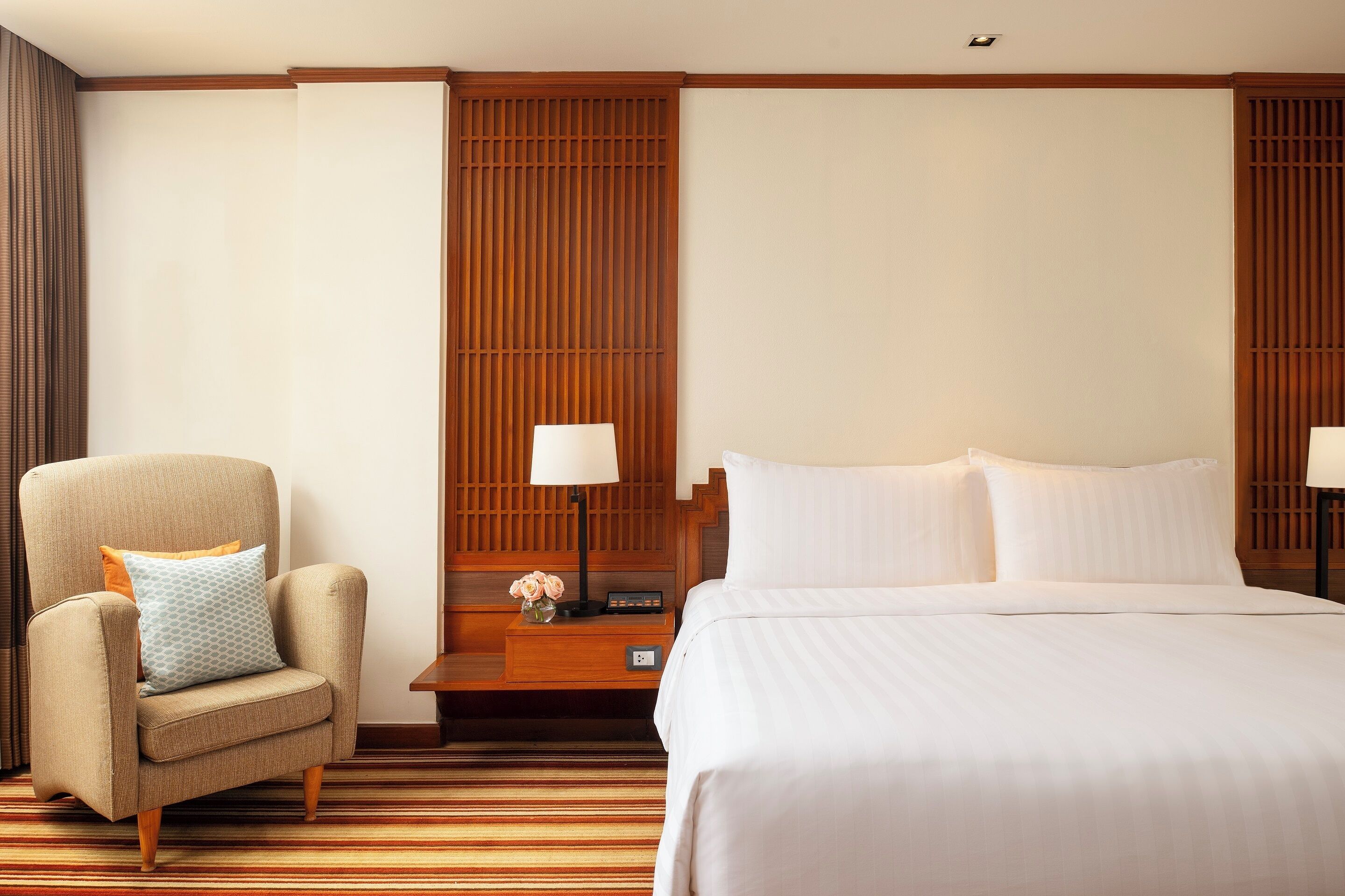 Een hotelkamer met een bed, een stoel, een nachtkastje en een wandpaneel.